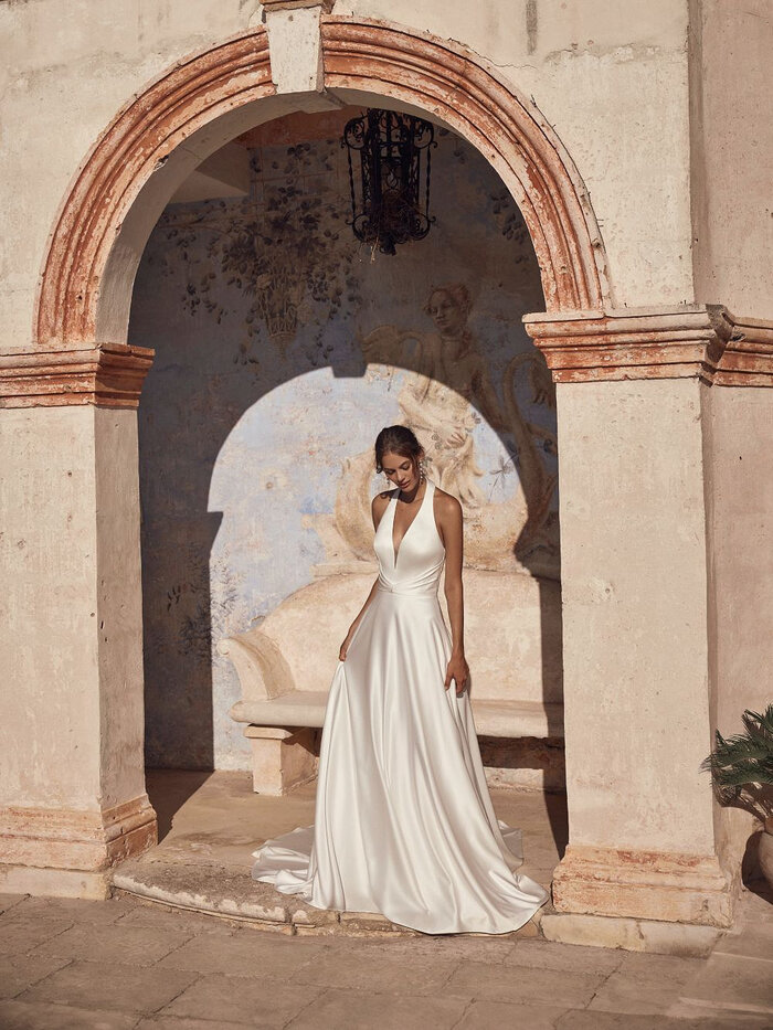 Das Brautkleid Milora D von Modeca Elegantes Brautkleid „Milora D“ von Modeca mit tiefem V-Ausschnitt, Neckholder, schmaler Taille und fließendem Rock