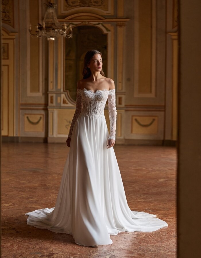 Das Brautkleid Sammi von Alberto Palatchi Brautkleid Sammi von Alberto Palatchi mit romantischem Off-Shoulder-Corsagenoberteil aus Spitze, langen transparenten Spitzenärmeln, betonter Taille und fließendem A-Linien-Rock mit Schleppe