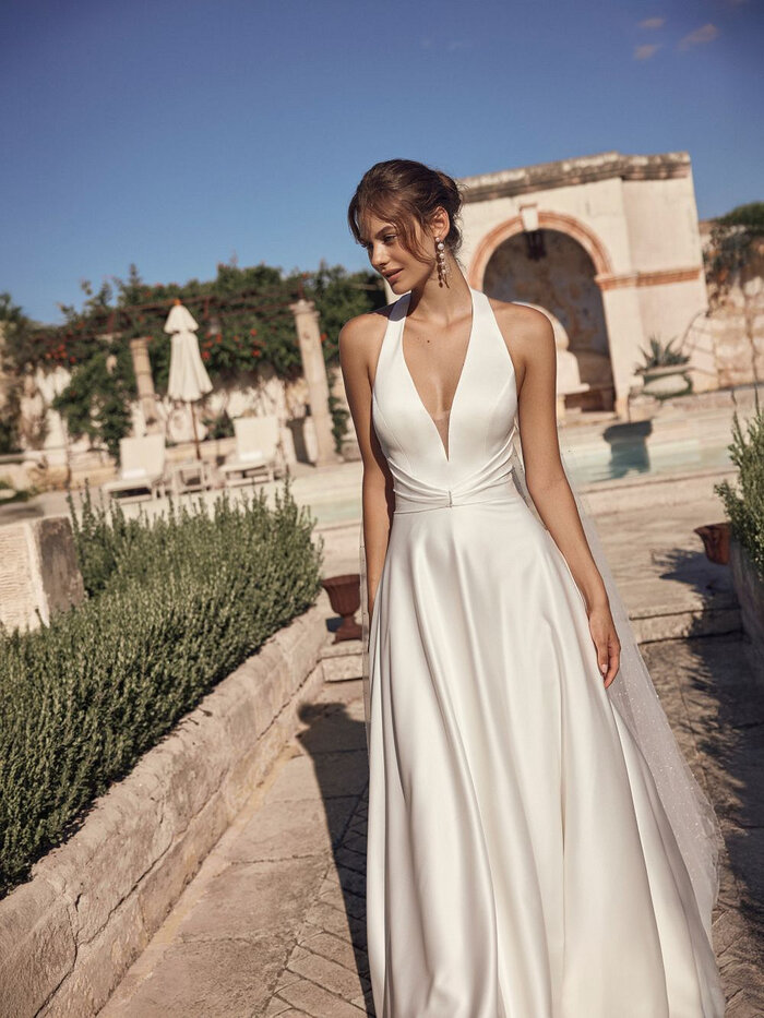 Das Brautkleid Milora D von Modeca Elegantes Brautkleid „Milora D“ von Modeca mit tiefem V-Ausschnitt, Neckholder, schmaler Taille und fließendem Rock