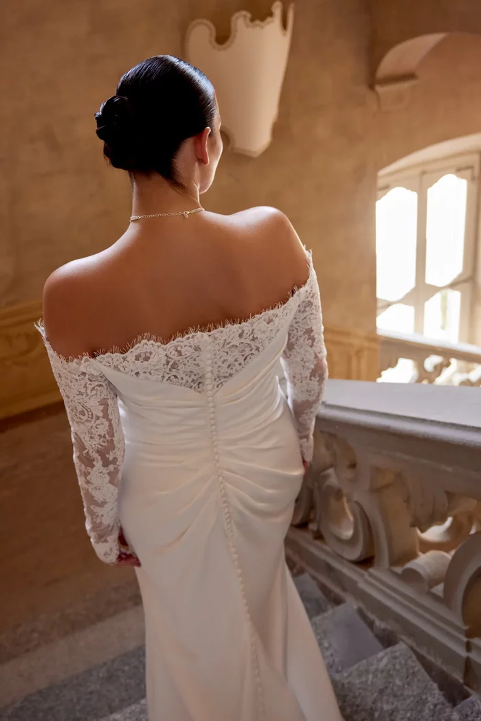 Curvy Brautkleid Jessa von Justin Alexander in der Rückenansicht mit schulterfreiem Ausschnitt, langen Spitzenärmeln, figurbetonter Fit-and-Flare-Silhouette und Beinschlitz – elegantes Plus-Size Hochzeitskleid in Ivory für moderne Bräute.