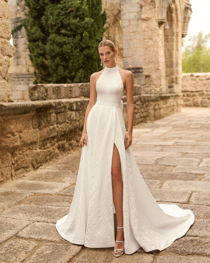 Das Brautkleid Prado von Adriana Alier Brautkleid Prado von Adriana Alier mit elegantem Neckholder-Ausschnitt, floraler Jacquard-Struktur und hohem Beinschlitz