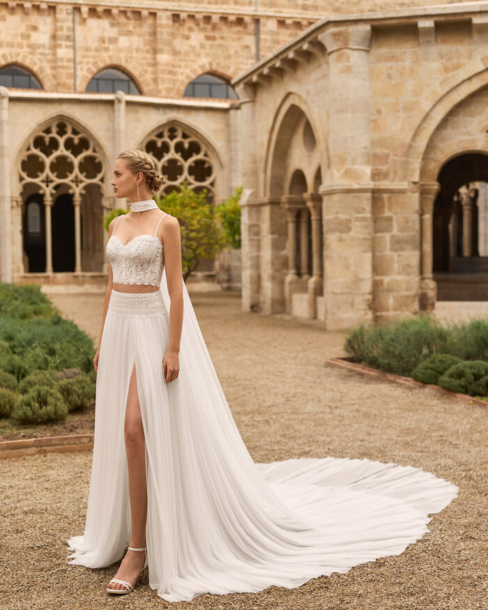 Ganzkörperaufnahme einer Braut vor einer Kathedrale, sie trägt das zweiteilige Brautkleid Livy, man sieht den Beinschlitz