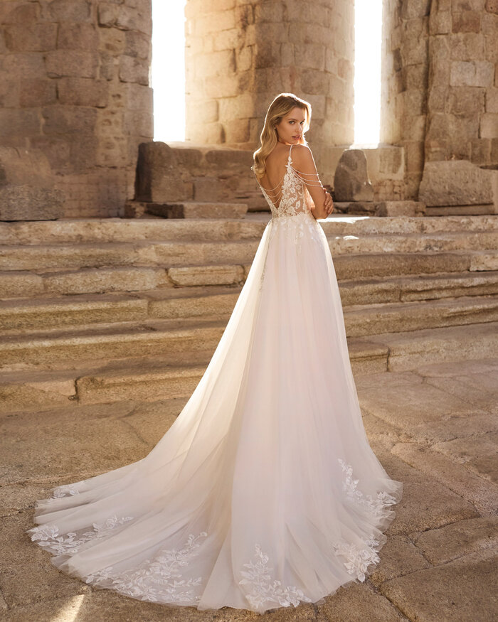 Brautkleid von Pinara von Adriana Alier Ganzkörperaufnahme einer Braut von hinten vor antiken Steinsäulen, sie trägt das Kleid Pinara von Adriana Alier, die Sonne scheint von hinten