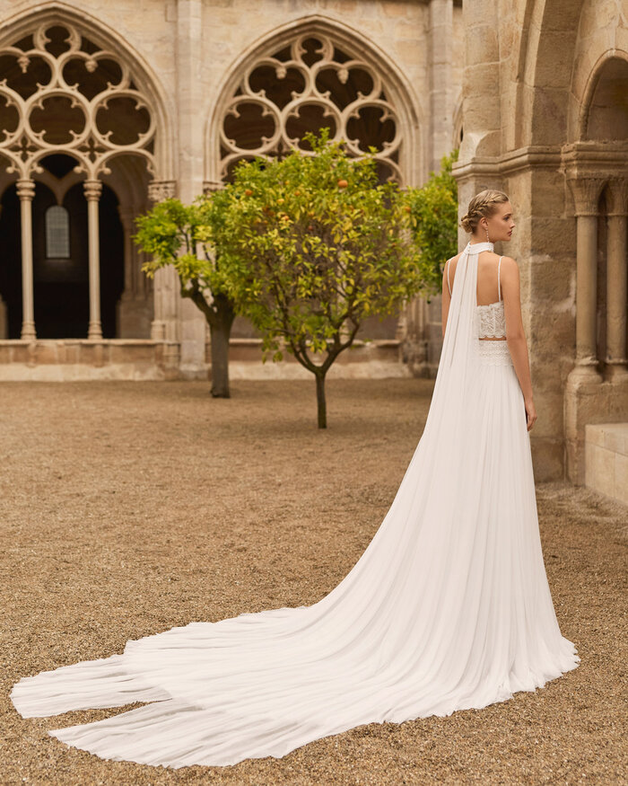 Ganzkörperaufnahme einer Braut von hinten vor einer Kathedrale, sie trägt das zweiteilige Brautkleid Livy, sie trägt ein schmales Cape aus Chiffon