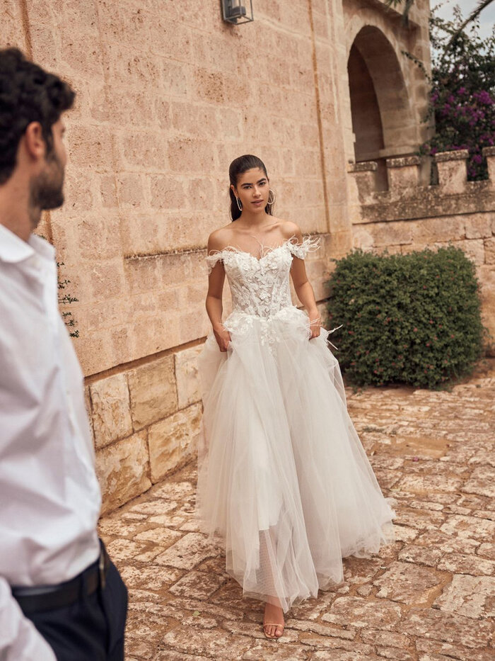 Das Brautkleid Merysol von Modeca Das Brautkleid Merysol von Modeca mit Tüllrock mit einem Perlen verzierten Spitzenoberteil und Federn