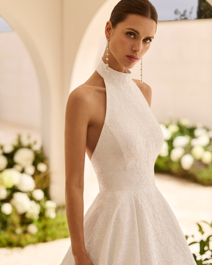 Das Brautkleid Nut von Rosa Clara Brautkleid Nut von Rosa Clará mit hochgeschlossenem Neckholder-Ausschnitt, eleganter Taillenbetonung und weit ausgestelltem A-Linien-Rock aus strukturiertem Stoff