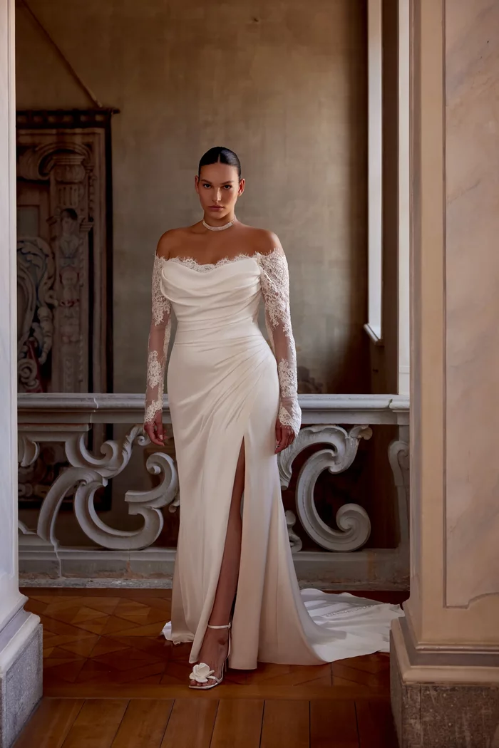 Curvy Brautkleid Jessa von Justin Alexander mit schulterfreiem Ausschnitt, langen Spitzenärmeln, figurbetonter Fit-and-Flare-Silhouette und Beinschlitz – elegantes Plus-Size Hochzeitskleid in Ivory für moderne Bräute.
