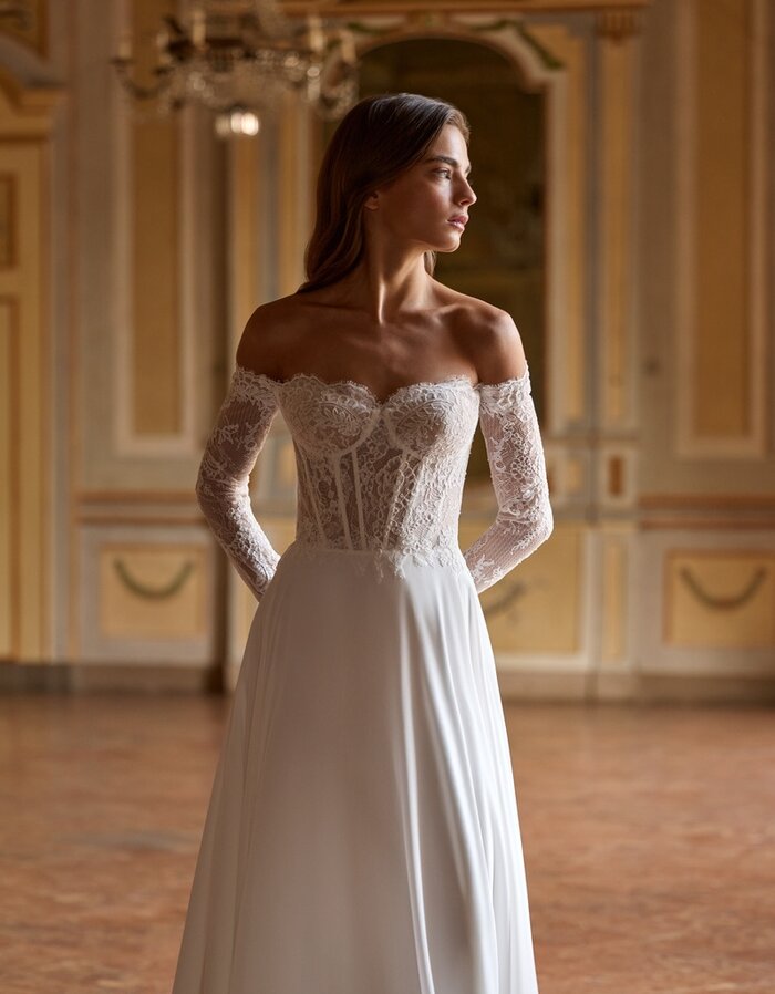 Das Brautkleid Sammi von Alberto Palatchi Brautkleid Sammi von Alberto Palatchi mit romantischem Off-Shoulder-Corsagenoberteil aus Spitze, langen transparenten Spitzenärmeln, betonter Taille und fließendem A-Linien-Rock mit Schleppe
