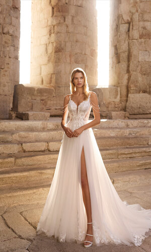 Brautkleid Pinara von Adriana Alier Ganzkörperaufnahme einer Braut vor antiken Steinsäulen, sie trägt das Kleid Pinara von Adriana Alier, die Sonne scheint von hinten, Braut zeigt den Schlitz im Kleid