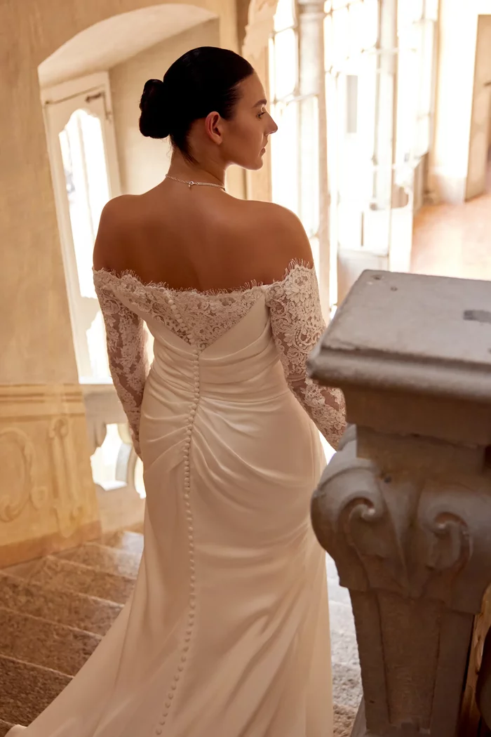 Curvy Brautkleid Jessa von Justin Alexander in der Rückenansicht mit schulterfreiem Ausschnitt, langen Spitzenärmeln, figurbetonter Fit-and-Flare-Silhouette und Beinschlitz – elegantes Plus-Size Hochzeitskleid in Ivory für moderne Bräute.