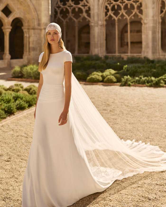 Ganzkörperaufnahme einer Braut vor einer Kathedrale, die Braut trägt das Kleid Lady von Adriana Alier 