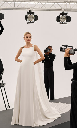 Brautkleid Scarlet von Adriana Alier Ganzkörperaufnahme einer Braut in einem Studio, sie trägt das Kleid Scarlet von Adriana Alier, 3 in schwarz gekleidete Fotografinnen richten Kameras und Scheinwerfer auf die Braut