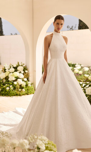 Das Brautkleid Nut von Rosa Clara Brautkleid Nut von Rosa Clará mit hochgeschlossenem Neckholder-Ausschnitt, eleganter Taillenbetonung und weit ausgestelltem A-Linien-Rock aus strukturiertem Stoff