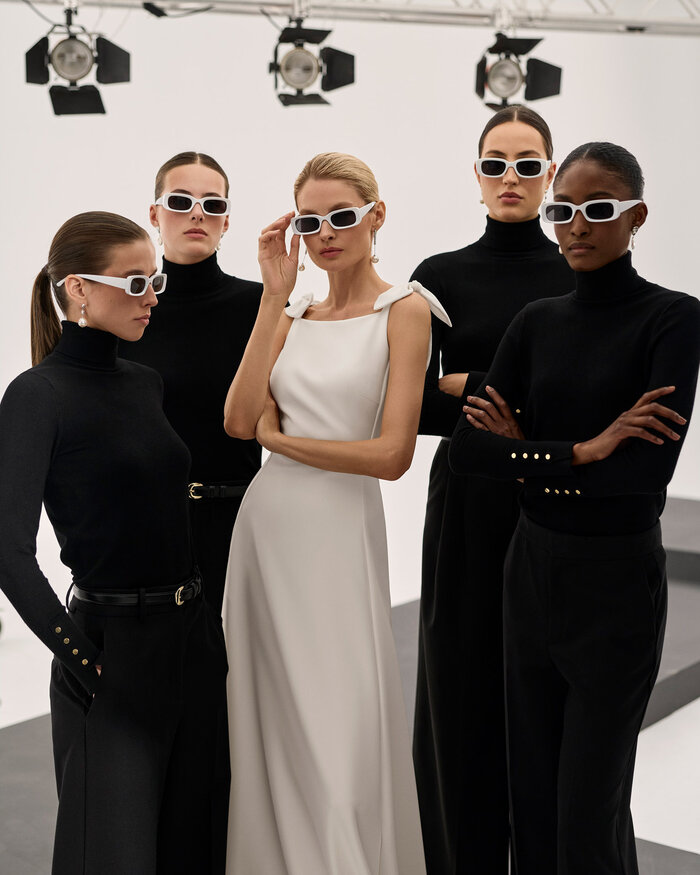 Gruppenfoto in einem Studio mit einer Braut und 4 in schwarz gekleideten Fotografinnen, die Braut trägt das Kleid Scarlet von Adriana Alier, alle 5 Frauen tragen eine weiße Sonnenbrille 