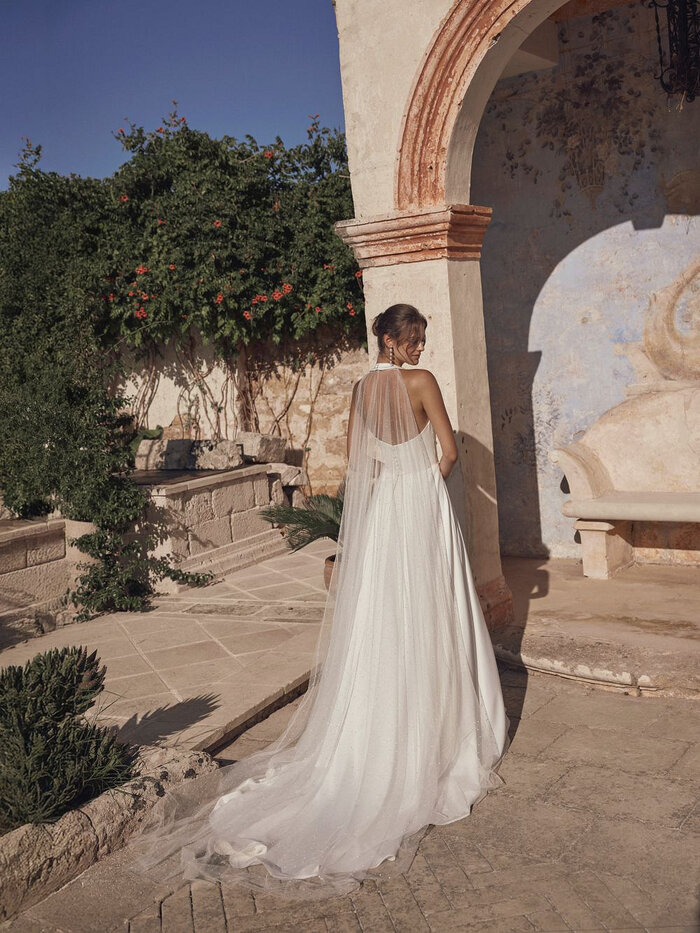 Das Brautkleid Milora D von Modeca Elegantes Brautkleid „Milora D“ von Modeca mit tiefem V-Ausschnitt, Neckholder, schmaler Taille und fließendem Rock mit Knopfleiste hinten in der Rückenansicht