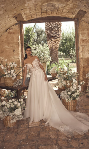 Brautkleid Mavisse von Modeca Romantisches A-Linien-Brautkleid mit floraler Spitze, schulterfreiem Corsagenoberteil und langer Schleppe in mediterranem Hochzeitsambiente.