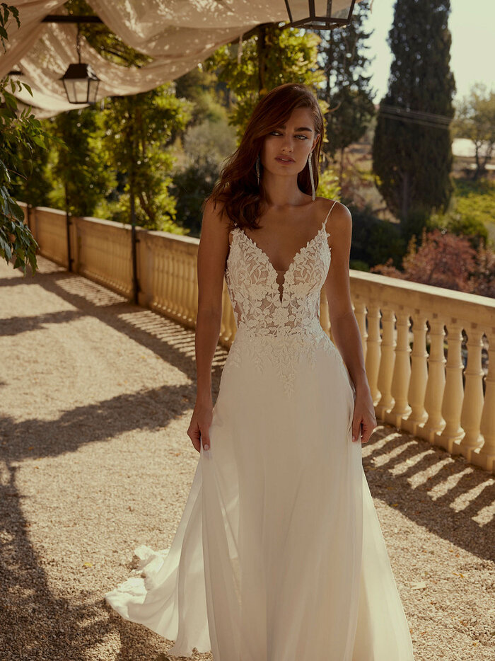 Das Brautkleid Debra von Modeca Elegantes Brautkleid „Debra“ von Modeca mit filigraner Spitze, tiefem V-Ausschnitt und fließendem Chiffonrock