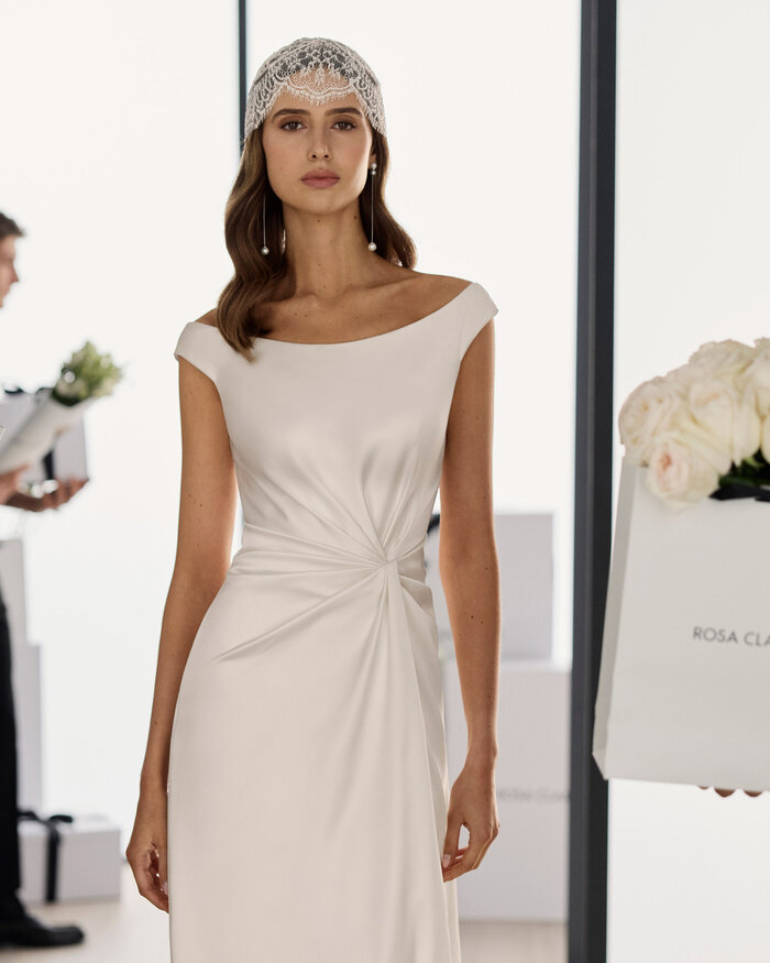 Nahaufnahme einer Braut im Studio, sie trägt das Brautkleid Solea von Adriana Alier, im Hintergrund befinden sich in schwarz gekleidete Männer die bei der Blumendeko helfen